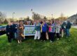A crowd standing around The Courtyard Memory Care Sign with a cut ribbon