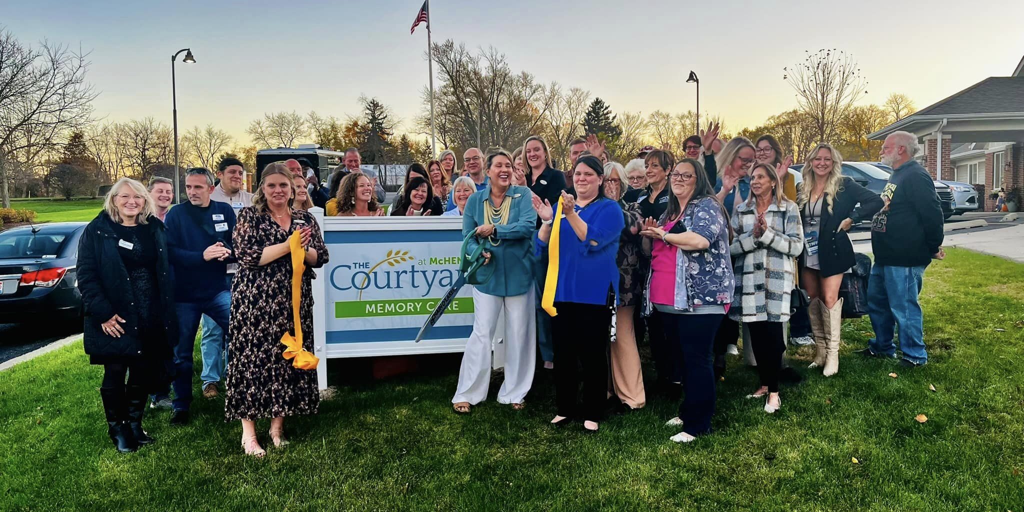 A crowd standing around The Courtyard Memory Care Sign with a cut ribbon