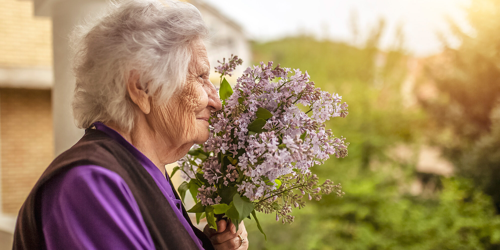 Senior woman smelling lilacs at a memory care community