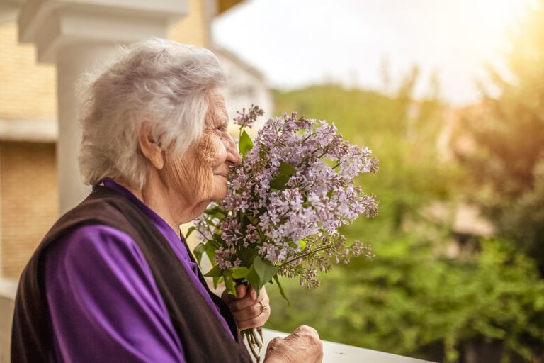 Senior woman smelling lilacs at a memory care community
